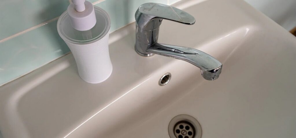 A modern chrome bathroom sink stopper sitting inside a white porcelain basin.