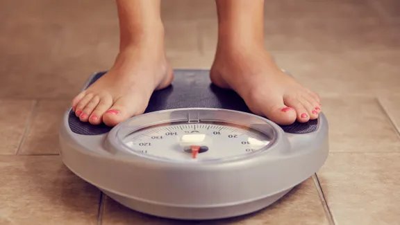 A person prepares to record their daily weight in a notebook on a bathroom floor.