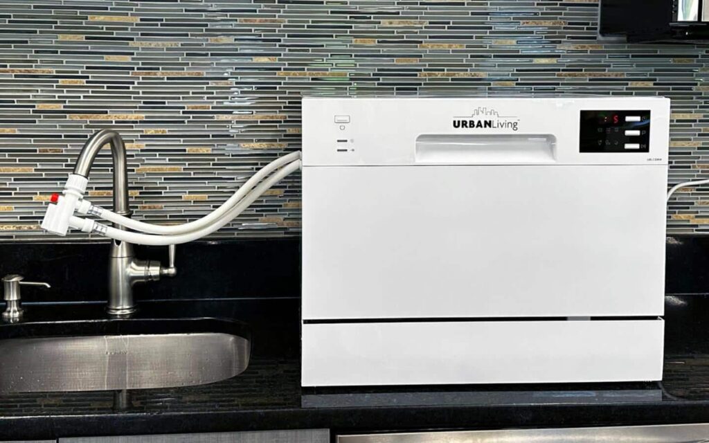 A countertop dishwasher connected to a kitchen faucet using a metal tap adapter.