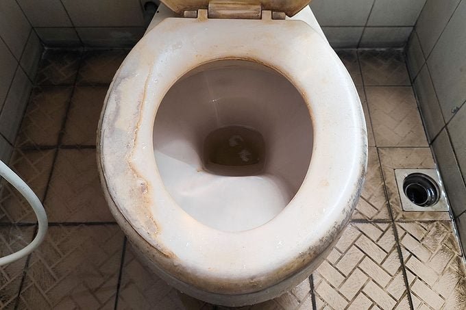 Close up of hands tightening a toilet seat hinge with a screwdriver.