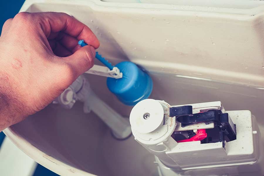 Hands using a wrench to repair the fill valve assembly of a toilet.