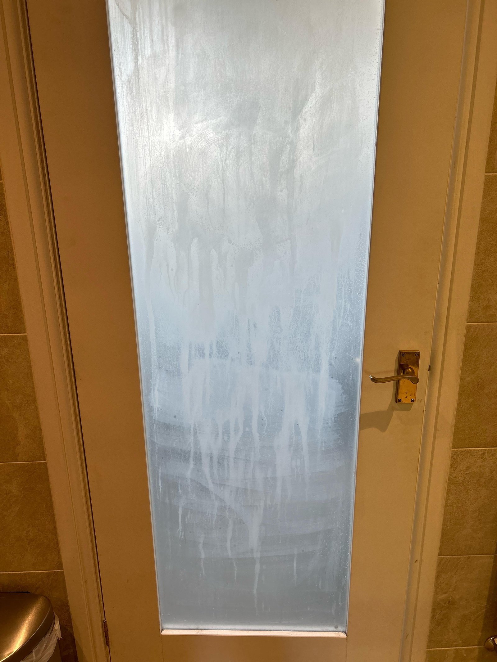 Fingertips test the smooth, clean surface of a frosted glass shower door.