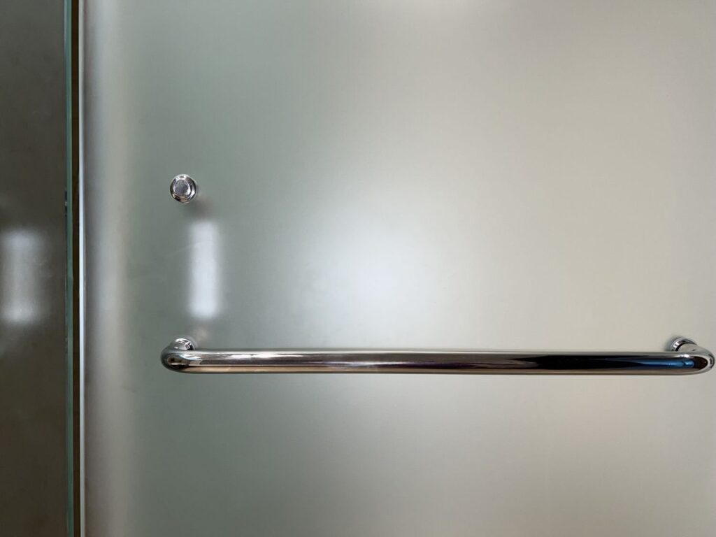 A clean frosted glass shower door stands in a bright, modern bathroom setting.