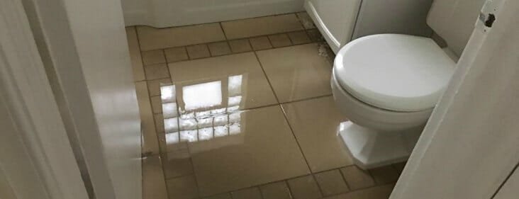 A flooded bathroom floor with water reflecting light in a clean, modern home.