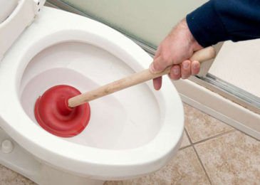 Hands performing a repair on a toilet fill valve by removing the cap.