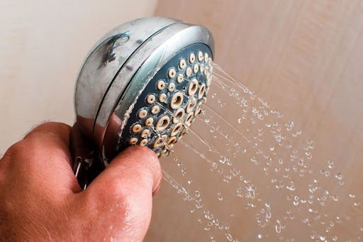 Close-up of limescale and mineral buildup clogging the holes of a showerhead.