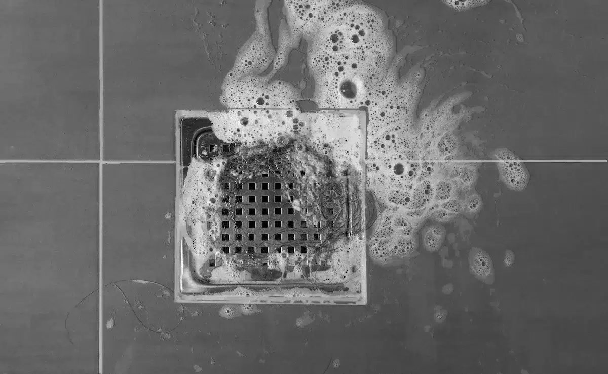 Pouring bleach into a shower drain to sanitize the plumbing.
