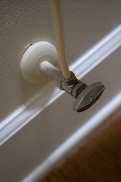 A hand turning the metal shutoff valve clockwise to stop the water.