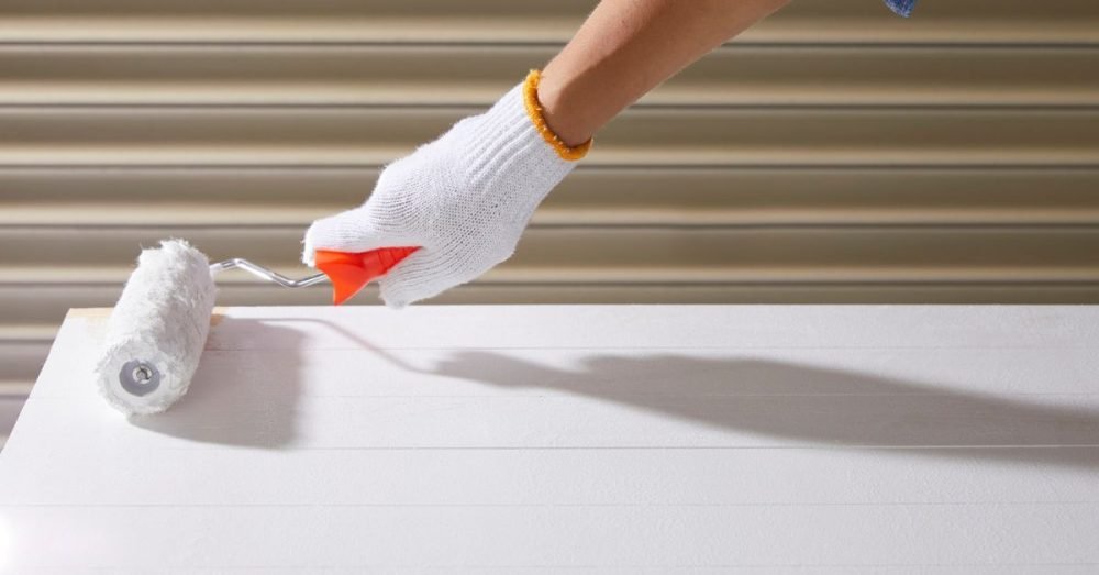 Hands repairing a section of blistered paint on a white interior wall.
