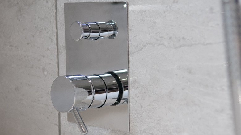 A close-up view of a chrome shower diverter button needing a repair.