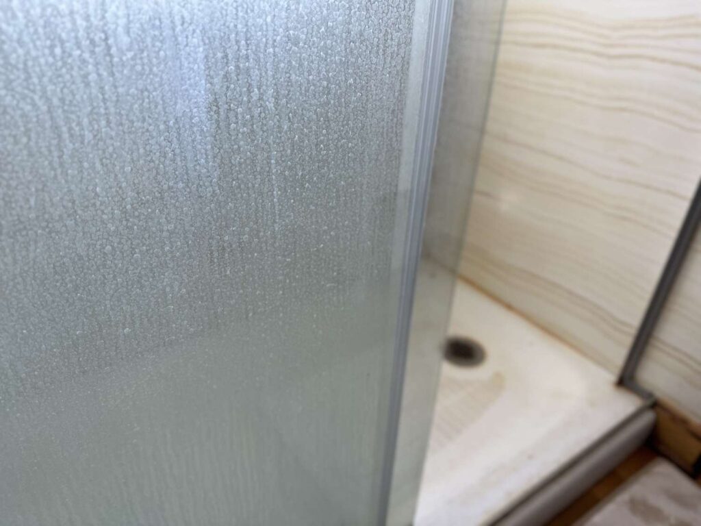 A clear glass shower door in a modern bathroom with natural lighting.