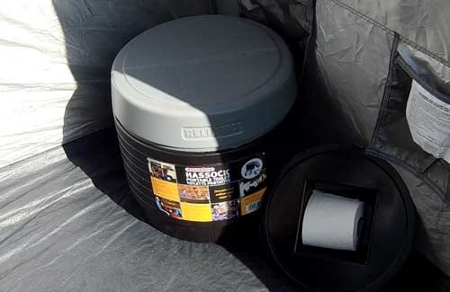 Reliance Hassock portable toilet placed in a serene forest campsite for outdoor convenience.