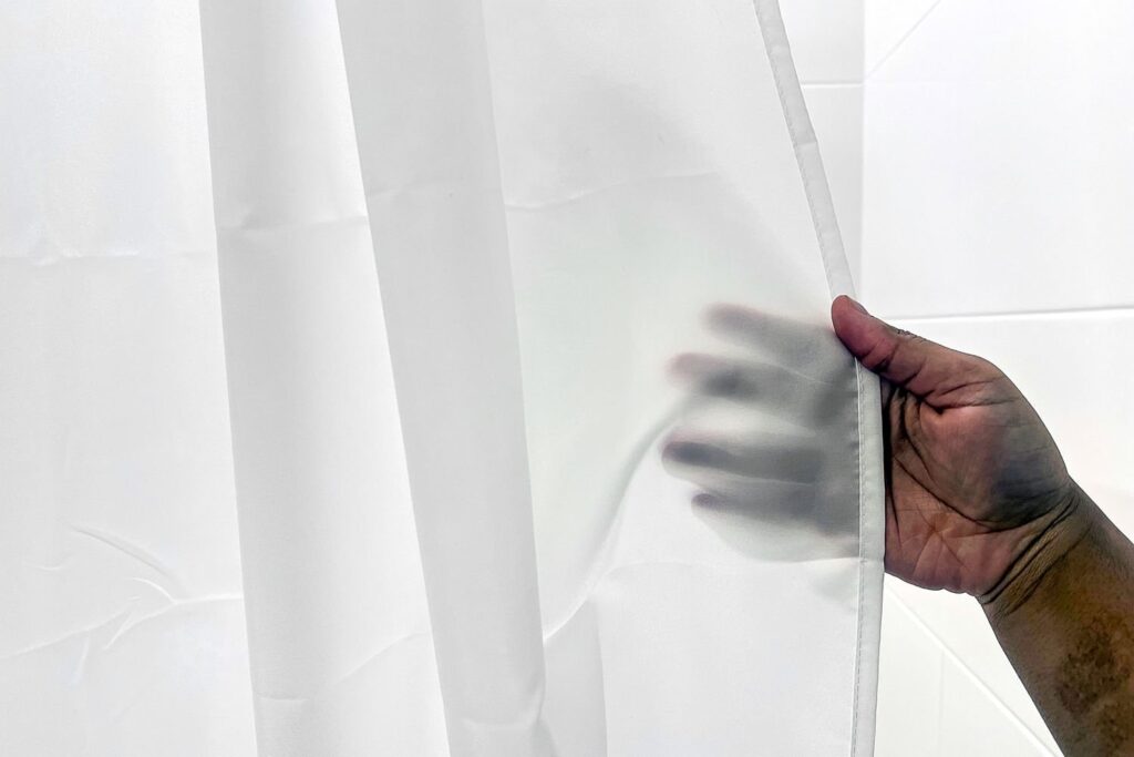 A clean fabric shower curtain hangs in a bright, modern bathroom setting.