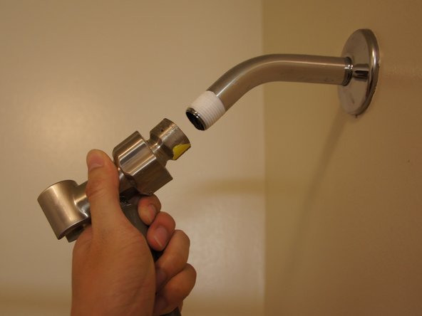 Close up of a shower arm connection showing worn tape and mineral buildup.