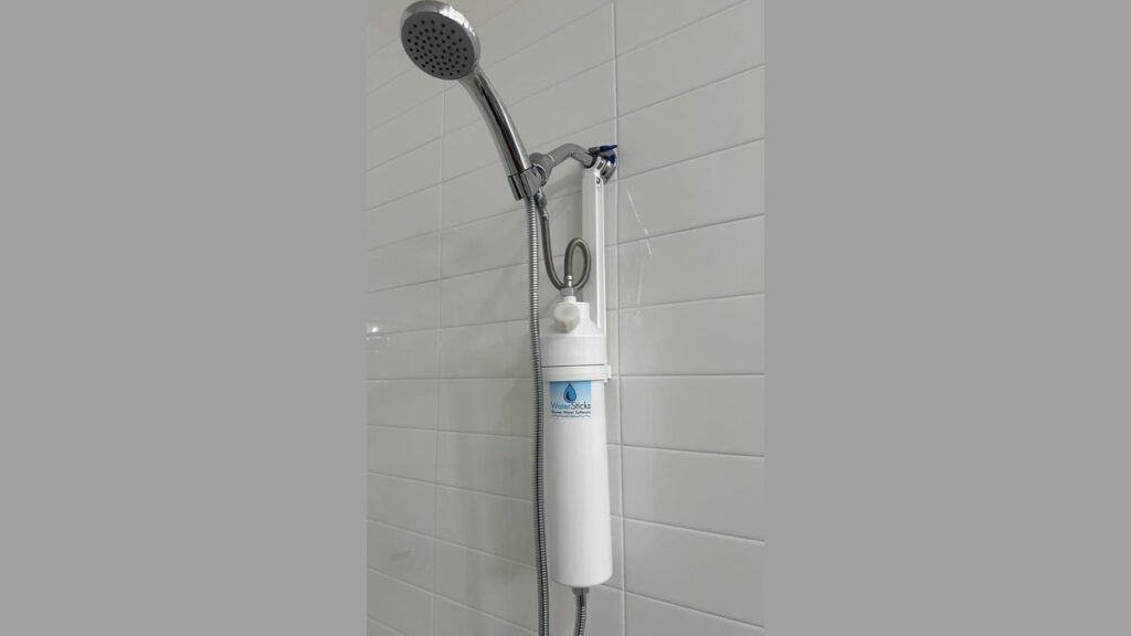 A modern shower water filter installed on a chrome shower head in a bathroom.