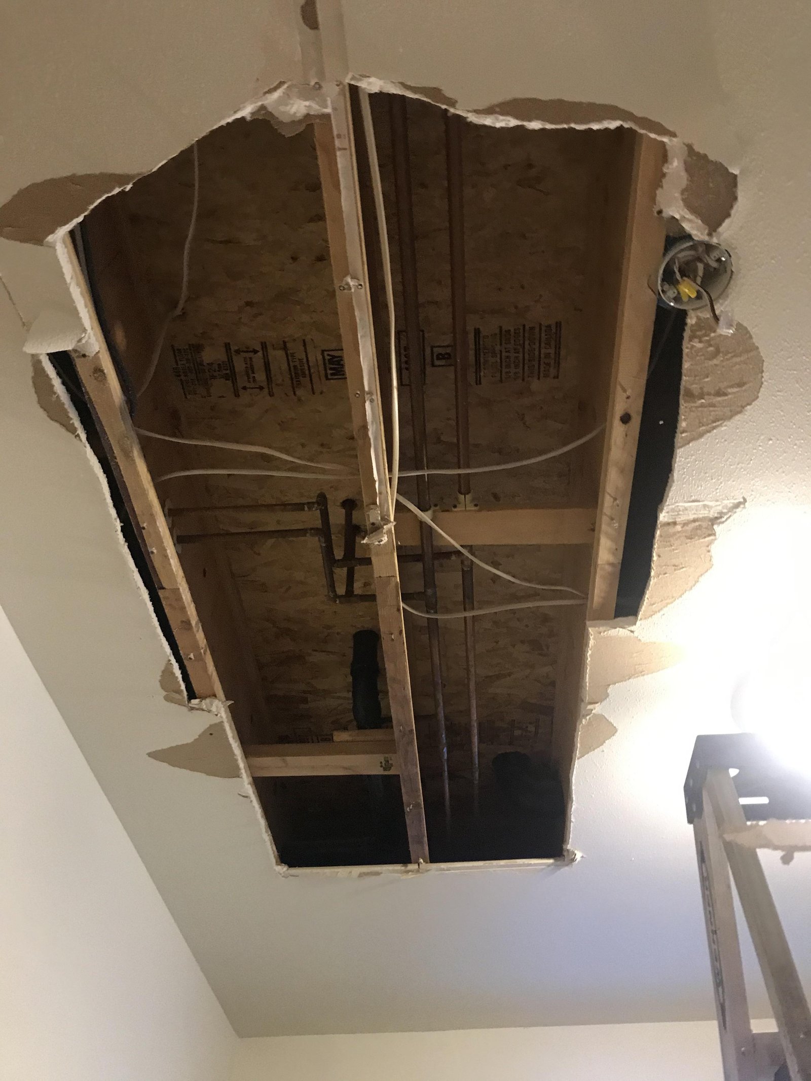 Hands turning a water shut-off valve to stop a bathroom ceiling leak.