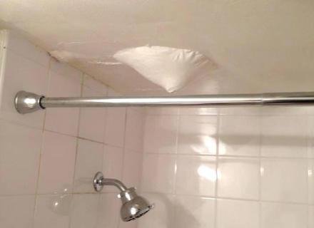 A water damaged ceiling dripping into a plastic bucket during a home flood.