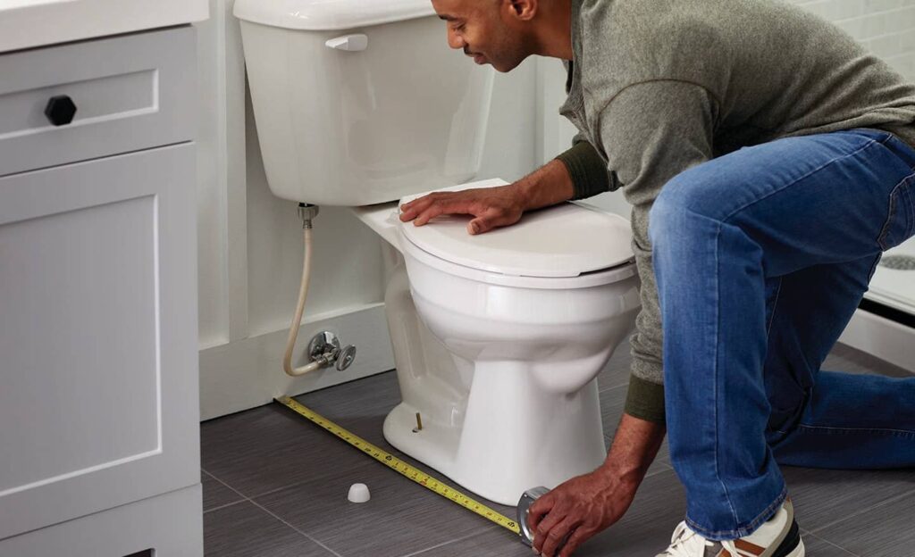 A professional plumber installing a new toilet in a bright modern bathroom.