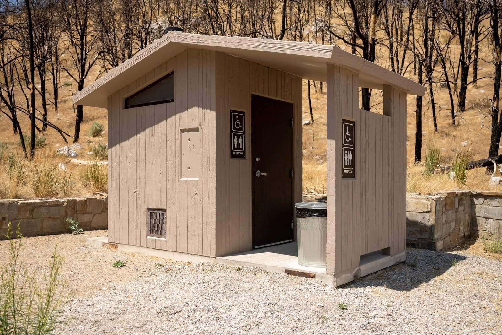 Interior view of a clean, functional vault toilet facility with a sanitizer dispenser.