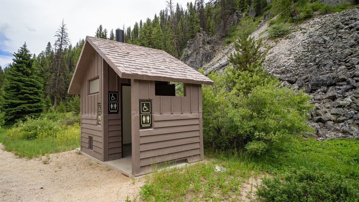 An elevated composting toilet structure built on rugged, rocky terrain in a park.