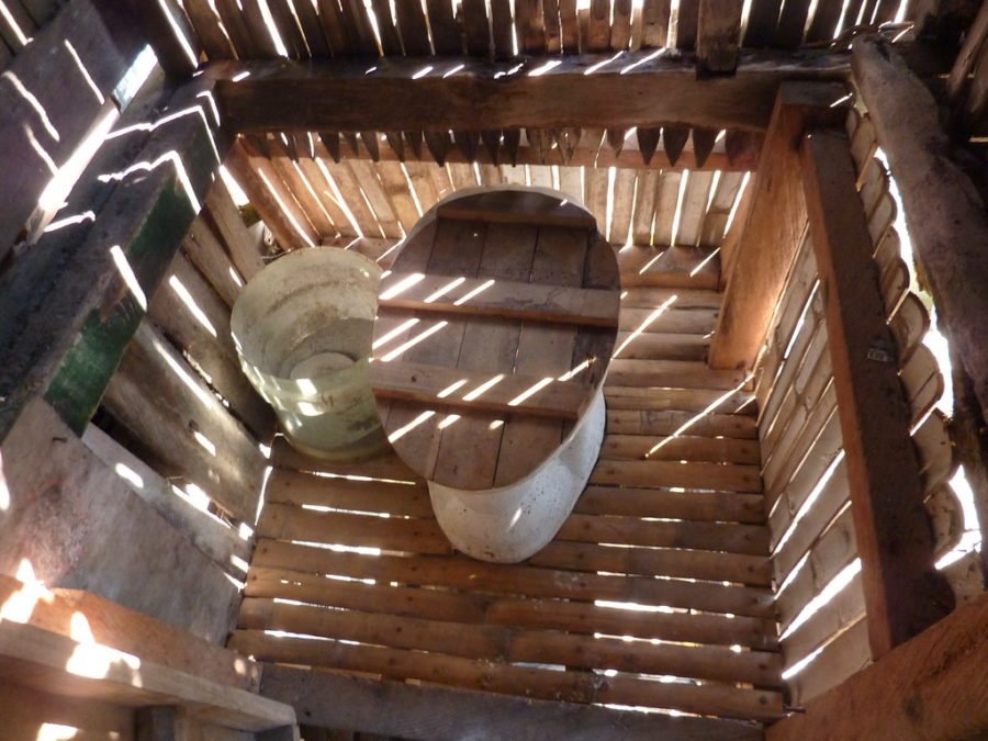 A park ranger standing near a vault toilet facility in a public campground.