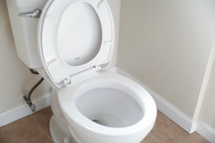 Measuring a toilet bowl rim with a tape measure to ensure the right seat size.